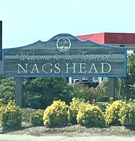 A Welcome Sign To The Town Of Nags Head In Front Of Some Bushes And Trees