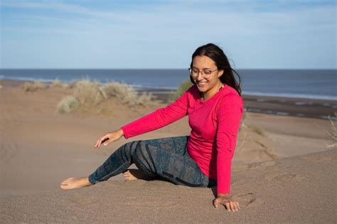 Una Mujer Latina Morena Sentada En Las Dunas Sonr E Con Indiferencia De Espaldas Al Mar Foto