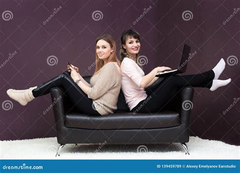 Two Girls Sit On The Couch With Their Backs To Each Other Stock Image