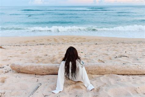 A menina senta se de costas para a câmera na areia da praia e olha para