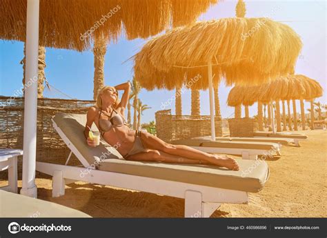 Sexy Woman Wearing Bikini Sitting On Lounger Under Straw Canopy