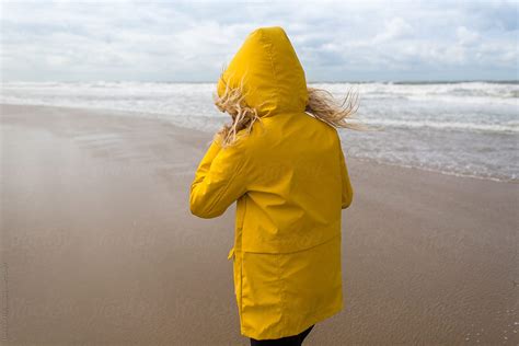 Woman On A Windy Beach Wearing A Yellow Raincoat By Stocksy