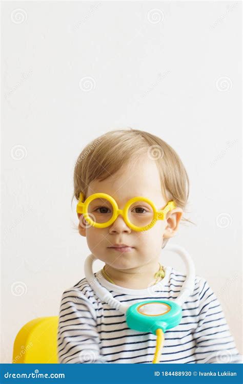 A Kid Play Doctor In The Nursery A Boy In Yellow Glasses Sits On The