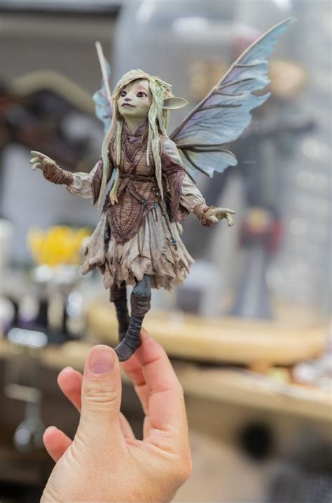 A Hand Holding Up A Tiny Fairy Figurine In The Shape Of A Doll