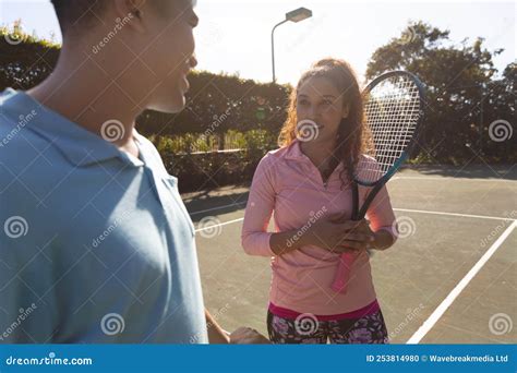 Smiling Biracial Couple Playing Tennis Talking Over The Net On Sunny