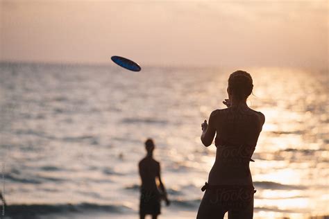 Friends On The Beach Playing Frisbee By The Sea By Stocksy