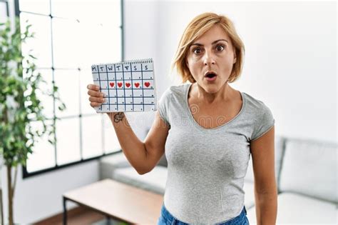 Middle Age Blonde Woman Holding Heart Calendar Scared And Amazed With Open Mouth For Surprise