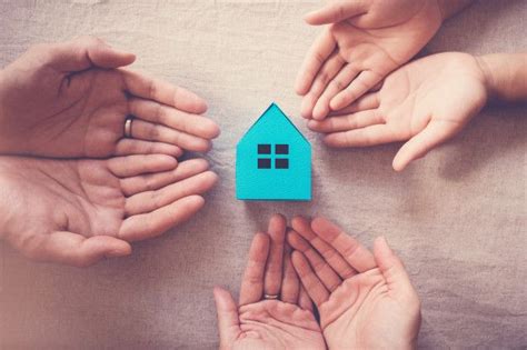 Several Hands Surrounding A Small Blue House On Top Of A Bed In Front