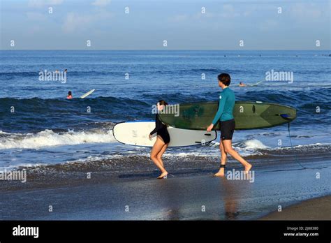 A Caucasian Couple Walking Into The Ocean Carrying Longboard Surfboards