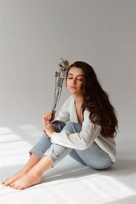 Charming Model Girl With Nude Makeup Wearing Jeans And Unbuttoned Blouse Posing With A Sprig Of