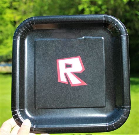 A Person Holding Up A Black Paper Plate With The Letter R On It In