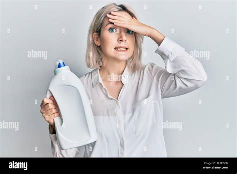 Jeune fille blonde tenant un flacon de détergent stressé et frustré avec la main sur la tête
