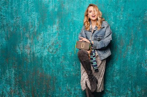 Sexy jolie femme blonde élégante en jeans et veste surdimensionnée marchant contre le mur vert
