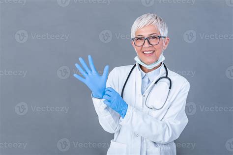 Senior Female Doctor Putting On Protective Gloves Isolated On