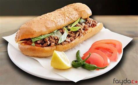 A Sandwich With Meat And Vegetables On A White Plate Next To Sliced