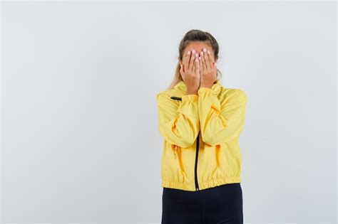 Femme Blonde Couvrant Le Visage Avec Les Mains En Blouson Aviateur Jaune Et Pantalon Noir Et à