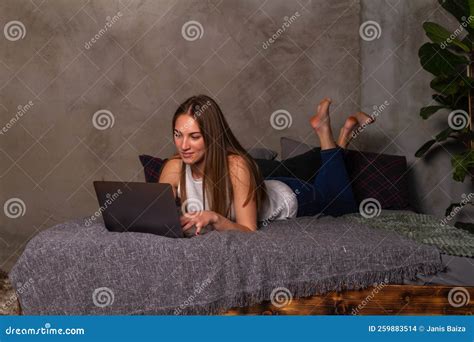 Woman Lying On Her Stomach In Bed And Working On A Laptop Stock Photo