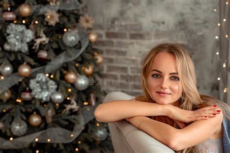 A Beautiful Blonde Is Sitting On A Sofa In A Room With Christmas Decorations Winter Mood Cozy