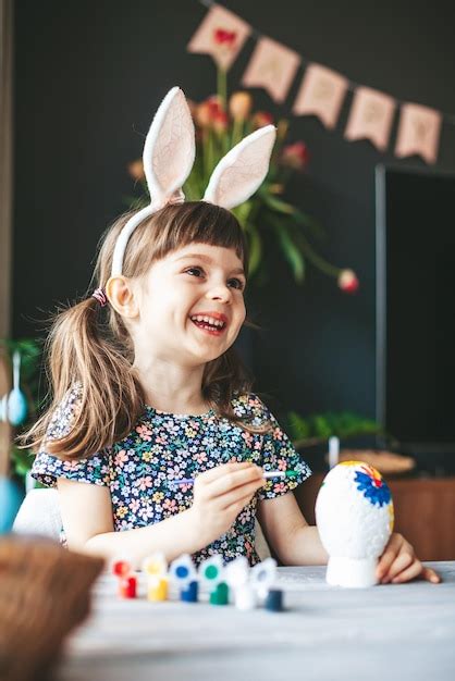 Niña feliz riéndose con orejas de conejo pintando huevos de pascua en