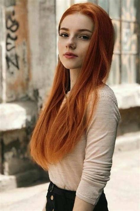 A Woman With Long Red Hair Standing In Front Of A Building And Looking