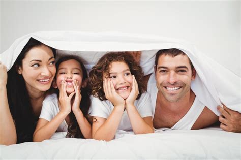 Familia Feliz Debajo De La Manta En La Cama En Casa Foto Premium