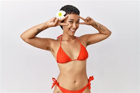 Junge hispanische Frau mit kurzen Haaren im Bikini macht ein Friedenssymbol mit den Fingern über