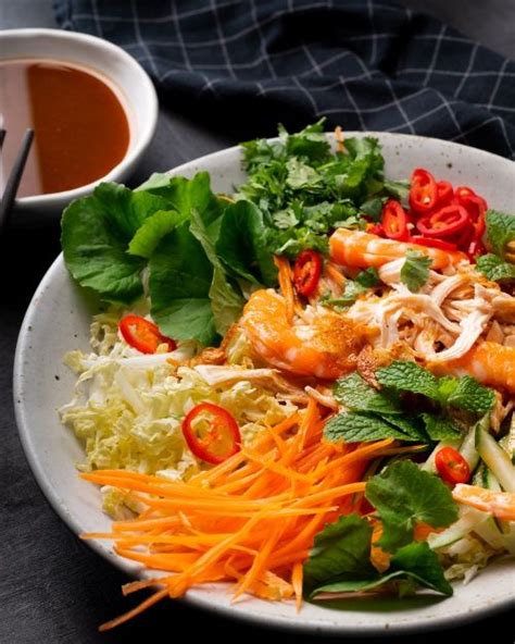 A White Plate Topped With Salad And Shrimp Next To A Cup Of Tea On A Table