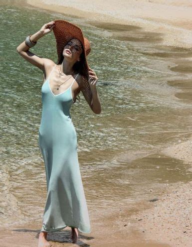 A Woman In A Blue Dress And Straw Hat Standing On The Beach With Her