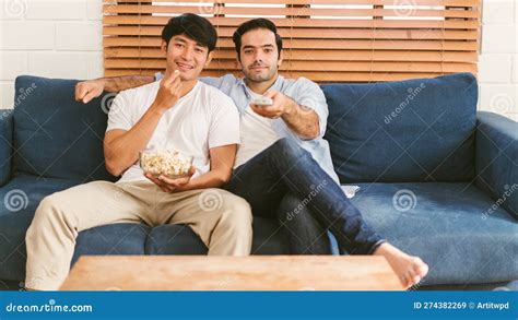 Gay Couple Sitting On The Sofa Having Popcorn And Enjoying Watching Content On The Tv In The