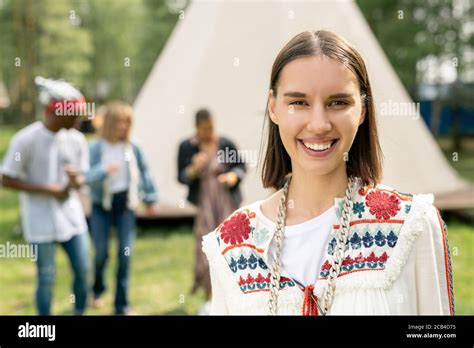 Portrait Of Cheerful Hippie Brunette Girl Standing Against Camping Tent And Dancing People Stock