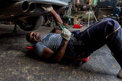 Mechanic Lying Down And Working Under Car At Auto Service Garage