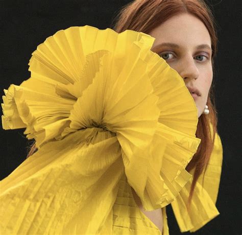 A Woman With Red Hair Holding A Large Yellow Flower In Front Of Her