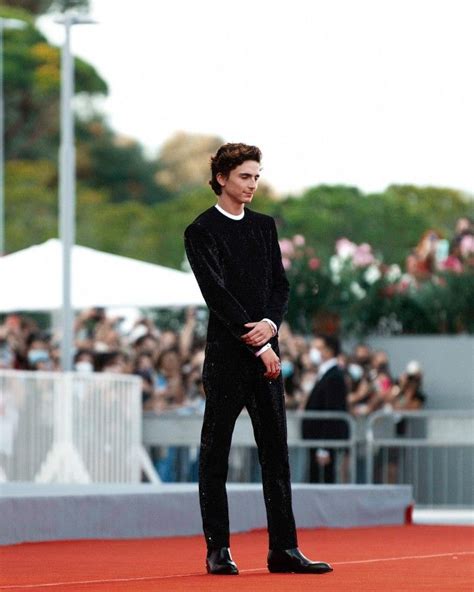 A Man In A Black Suit Standing On Top Of A Red Carpet Next To A Crowd