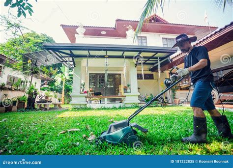 Asian Man Mowing Lawn In The Garden With Blurry House Mowing Or