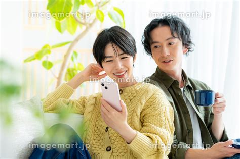 リビングでくつろぎながらスマホを見る若い日本人カップル （人物）の写真素材 243014363 イメージマート