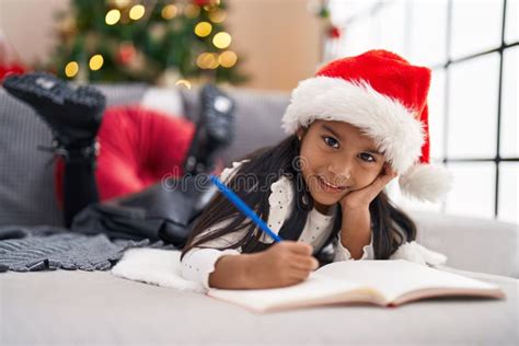 Adorable Hispanic Girl Drawing On Notebook Lying On Sofa By Christmas