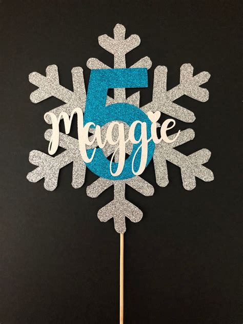 A Snowflake Shaped Cake Topper With The Number Five On It