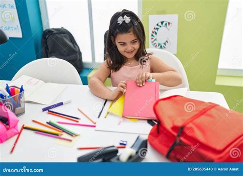 Adorable Hispanic Girl Student Sitting On Table Holding Book At