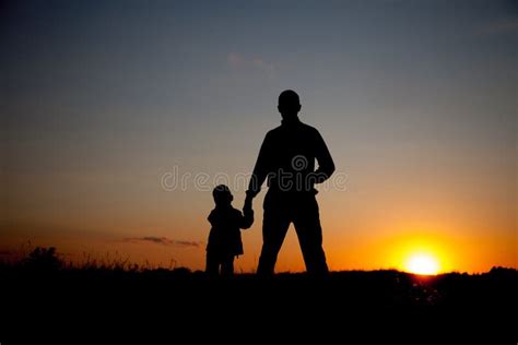 Silhouette Of Father And Son Holding Hands At Sunset Stock Photo