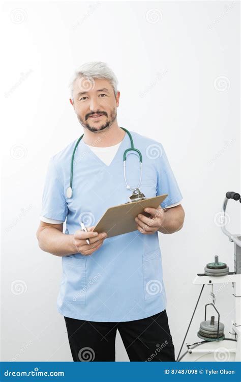 Male Doctor Holding Clipboard While Standing In Hospital Stock Photo