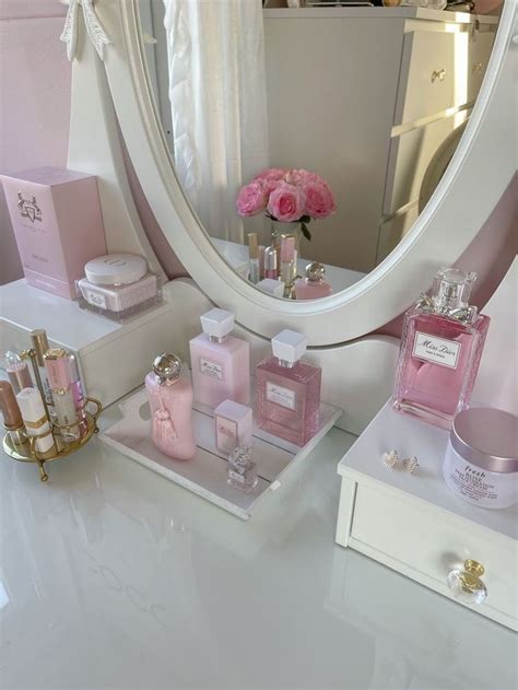 A White Vanity Topped With Lots Of Pink Perfumes And Bottles Next To A