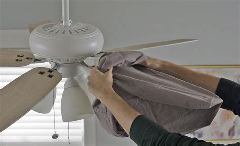 Person sliding a pillowcase over a dusty ceiling fan blade to capture dust easily