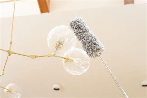 Microfiber cloth dusting a ceiling light fixture while standing on a stable step ladder